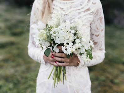 Bride standing in white dress holding flowers.