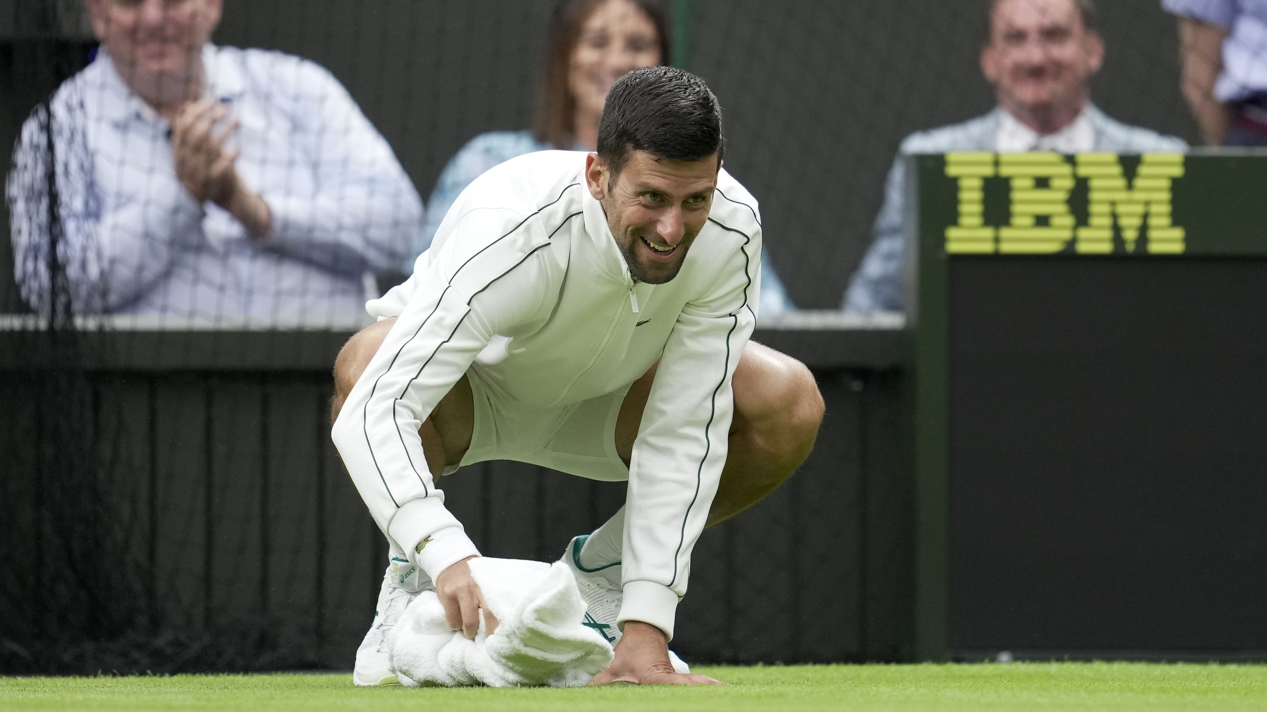Novak Djokovic wipes the court with his towel after rain fell on day one, much to the amusement of courtside fans.