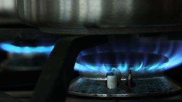 A gas flame burns under a pot on a gas stove top.