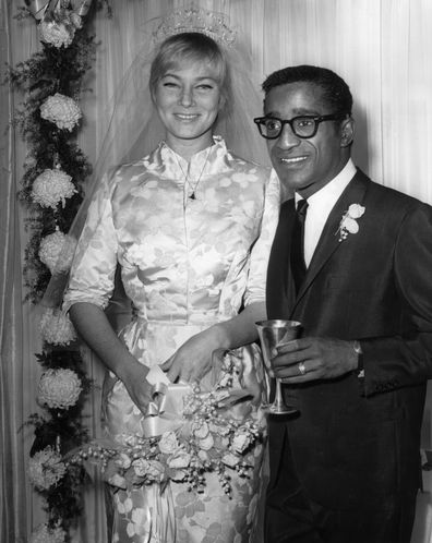 13th November 1960:  American actor, singer and dancer Sammy Davis Jr. (1925  - 1990) stands next to his wife, Swedish actor May Britt, at their wedding reception at Davis's home, Hollywood, California. Britt wears a silk brocade wedding gown with a veil and bouquet. Davis wears a suit and holds a goblet.  (Photo by Hulton Archive/Getty Images)