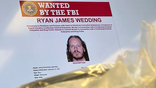 FILE - An image of former Canadian Olympic snowboarder Ryan Wedding, who is a fugitive and been charged with allegedly running and participating in a transnational drug trafficking operation, is displayed on a video monitor along with bricks of cocaine, foreground, during a news conference at the FBI offices in Los Angeles, Oct. 17, 2024. (AP Photo/Damian Dovarganes, File)