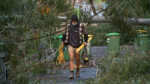 A man carrying tools walks through a street ravaged by wild weather that struck parts of Victoria.