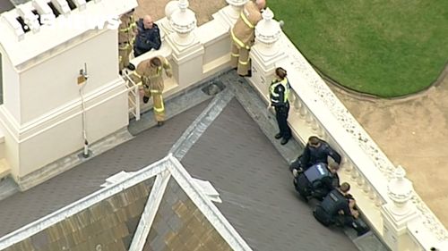 Police arrest a man on the roof of Government House.