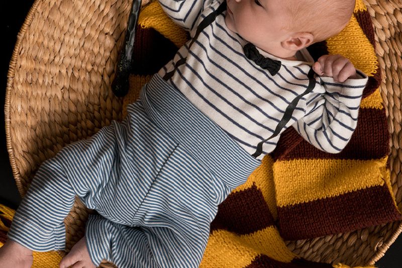 Baby lying in basket with red and yellow scarf and wand.