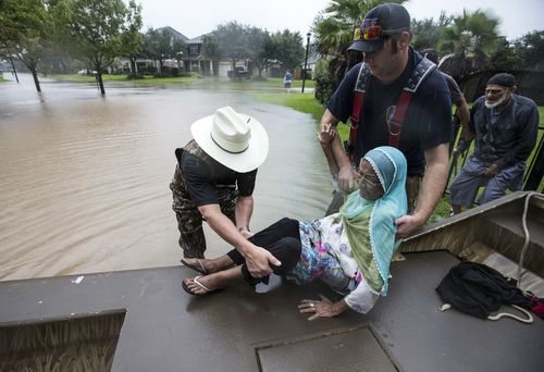 Fort Bend County Sheriff Troy Nehls, left, helps Mumtaz Kara and her husband, Tarmohamed Kara, far right, from rising waters. (AAP)