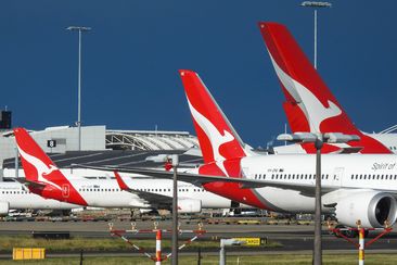 The vertical stabilisers of Qantas planes at Sydney Kingsford-Smith Airport, from the left: a Boeing B737-838 plane, registration VH-XZD; a Boeing B787-9 plane, registration VH-ZNE; and an Airbus A380-842 plane, registration VH-OQB. In the background on the left is a fourth Qantas plane, a Boeing B737-838, registration VH-XZH. In the far background is the international terminal.  In the foreground are navigational light structures at the northern end of the runway.  This image was taken from Nig