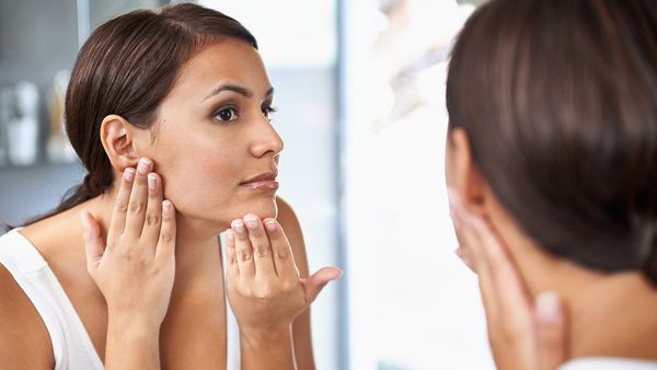 A beautiful young woman looking at her face in the mirror