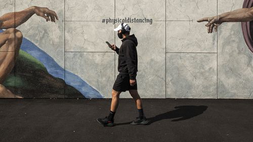 A man wearing a mask walks past street art in South Melbourne