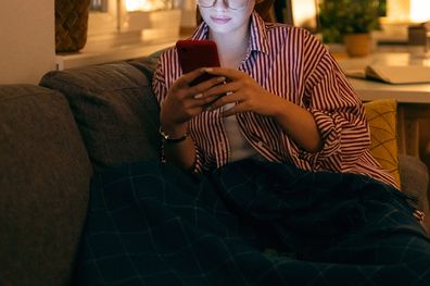 Stock image of woman sitting on lounge scrolling through her phone