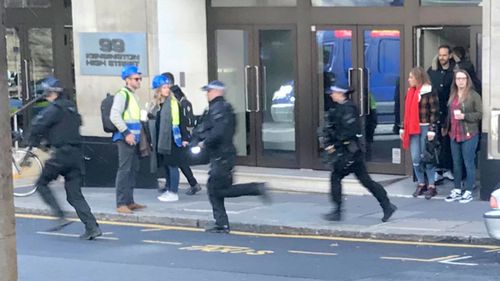 People watch as armed police officers run to the scene of an incident in central London amid reports a man with a machete has entered the Sony Music headquarters.