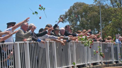 People gather at Bold Street Bridge in western Sydney for the traditional throwing of roses onto the train tracks below, as they commemorate the 32nd anniversary of the Granville Train Disaster