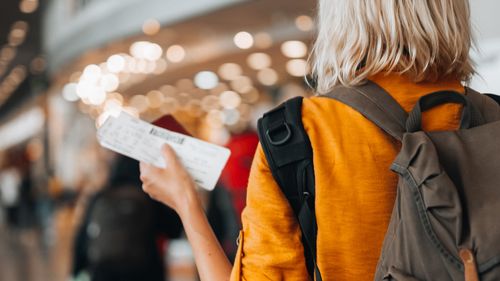 Rear view of a  woman at the airport holding a passport with a boarding pass as she walks to her departure gate