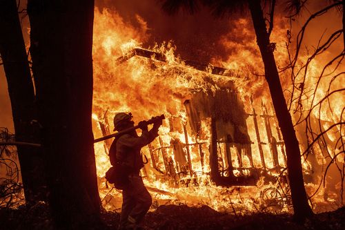 Firefighter Jose Corona sprays water as flames consume from the Camp Fire consume a home in Magalia.