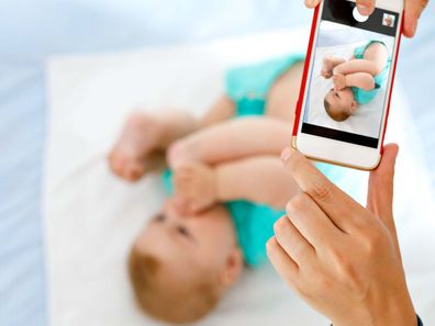 Baby lying down being photographed on phone.