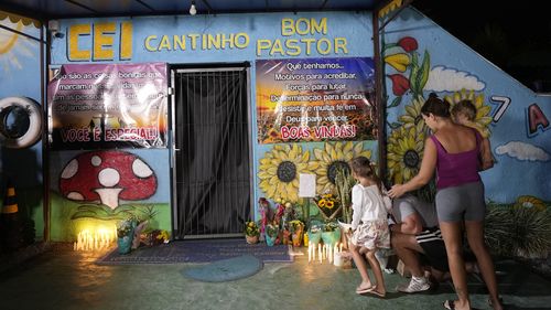 A family lights a candle at a makeshift memorial at the "Cantinho do Bom Pastor" daycare center after a fatal attack on children in Blumenau, Brazil, 