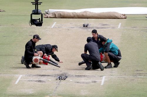 Farcical scenes this morning as groundsmen frantically try to dry out the pitch after wet got under the covers overnight. Picture: AAP