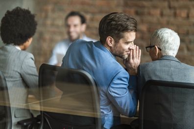 Back view of male member of human resource team whispering something to his colleague during a job interview in the office. The view is through glass.