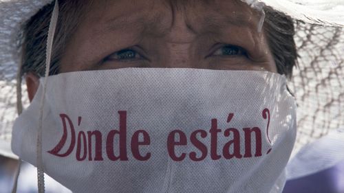 A mother with a face mask that reads in Spanish "Where are they?" marches along with hundreds of other mothers holding images of their missing relatives during Mother's Day, in Mexico City, Sunday, May 10, 2015. Mothers and other relatives of persons gone missing in the fight against drug cartels and organized crime are demanding that authorities locate their loved ones.