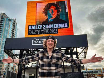 Bailey Zimmerman poses in front of a Billboard promoting his single.