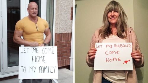 Mr and Mrs Tomlinson carrying signs as part of the #letthemcomehome campaign taken up by the thousands of temporary residents trying to get back to Australia.