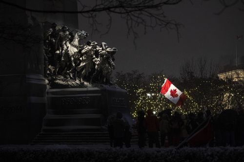 Protesters fly the Canadian flag as they stand by the Tomb of the Unknown Soldier at the National War Memorial on the 21st day of a protest against COVID-19 measures that has grown into a broader anti-government protest, on Thursday, Feb. 17, 2022, in Ottawa.