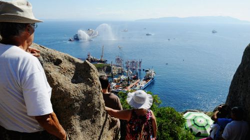 Onlookers watch as the wrecked cruise ship Costa Concordia is towed by tugs from Giglio after being refloated.