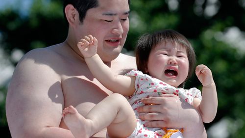 A baby breaks into tears as a wrestler picks her up. (AAP)