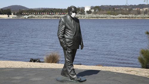 A statue of former Prime Minister Sir Robert Menzies seen wearing a face mask, along Lake Burley Griffin in Canberra.