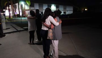 Bystanders comfort each other as they stand near a business building where a shooting occurred in Orange, California.