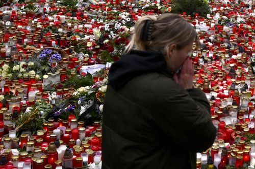 A young woman reacts by the floral tributes and candles left outside the headquarters of Charles University in downtown Prague, Czech Republic, Saturday, Dec. 23, 2023.  