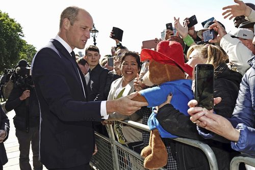 Prince William shakes hands with a Paddington Bear toy as he meets members of the public .