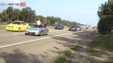 Two men throw bottles from the sun roof of a car at a mobile speed camera van parked on Foreshore Drive in Botany, Sydney. (9NEWS)