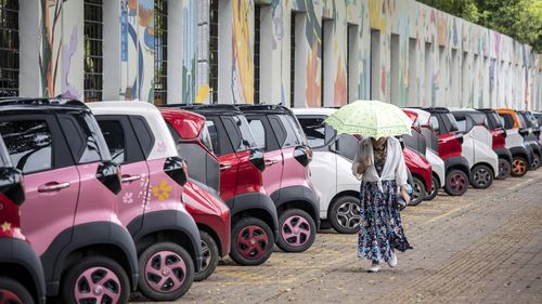 A women walks past SAIC-GM-Wuling Automobile Co. electric vehicles at a roadside parking lot in Liuzhou, China.