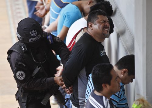An alleged member of the Mara Salvatrucha gang is handcuffed by a policeman of the anti-gang unit while lined-up against a wall next to other suspects during a police raid in San Salvador, El Salvador.