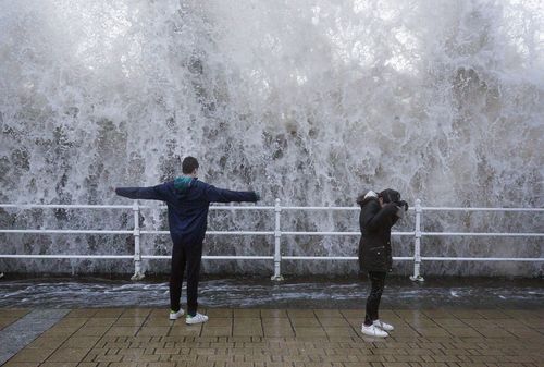 Children stand on the seafront as a wave crashes over the sea wall in Aberystwyth in west Wales. (AAP)