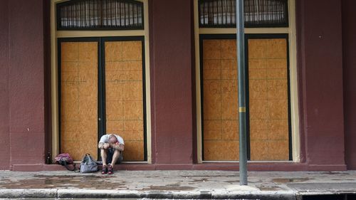 A man sits in front of a French Quarter business with windows boarded in preparation Hurricane Ida. (AP Photo/Eric Gay)