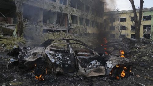 Samochód płonie przed szpitalem położniczym zniszczonym w wyniku bombardowania w Mariupolu na Ukrainie. 