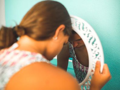 A teenage girl toucher head to the mirror looking sad