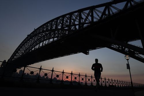 A jogger runs along Sydney Harbour under the Sydney Harbour Bridge against the backdrop of a stunning sunrise created by smoke haze from hazard reduction burns in Sydney. (AAP)