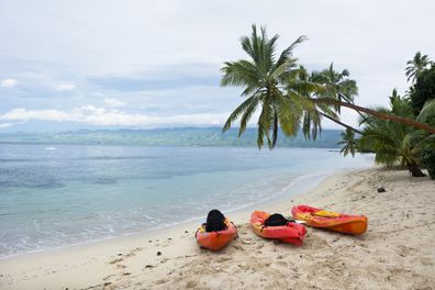 Three orange kayaks sit on a resort beach on an exotic island in Fiji.