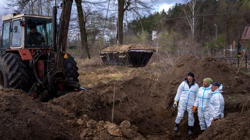 A crane lifts a casket as volunteers remove the soil from a mass grave during an exhumation of four civilians killed in Mykulychi, Ukraine