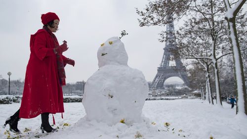 Decked out in red, a woman dresses a snowman on the snow-covered Trocadero. (AAP)