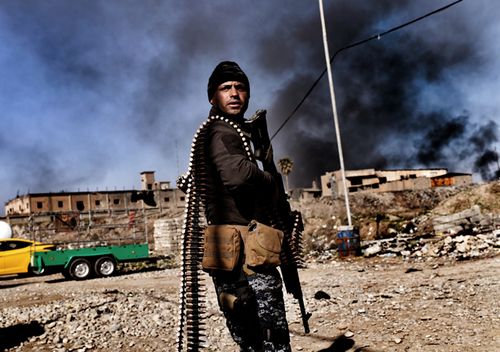 Smoke rises in the background as members of Iraq's elite Rapid Response Division hold position in the northern city of Mosul, on February 25, 2017. (AFP)