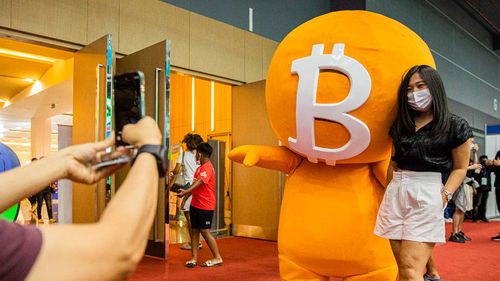 A woman poses with a Bitcoin mascot at a cryptocurrency expo in Bangkok, Thailand.