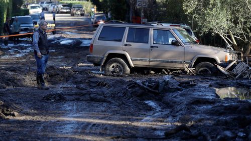 A man stands on a muddy road damaged from storms. (Image: AAP)