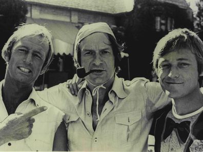 Paul Hogan (left) and John Cornell (right) get Hugh Hefner (centre) to wear Strop's signature cap in 1986.