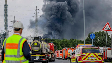 Emergency vehicles of the fire brigade, rescue services and police stand not far from an access road to the Chempark over which a dark cloud of smoke is rising in Leverkusen, Germany, Tuesday, July 27, 2021