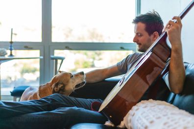 Man singing to dog. Man singing with dog. Man sitting on couch with dog. Man playing guitar.
