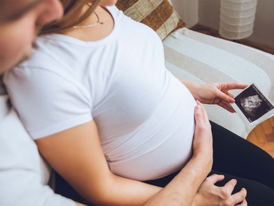 Man holding pregnant wife from the back as they look at ultrasound picture.