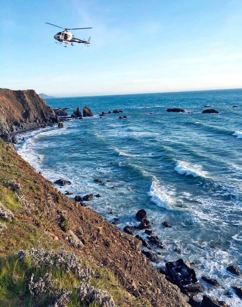 A helicopter hovering over steep coastal cliffs near Mendocino, California where the SUV went off the road. (AP)